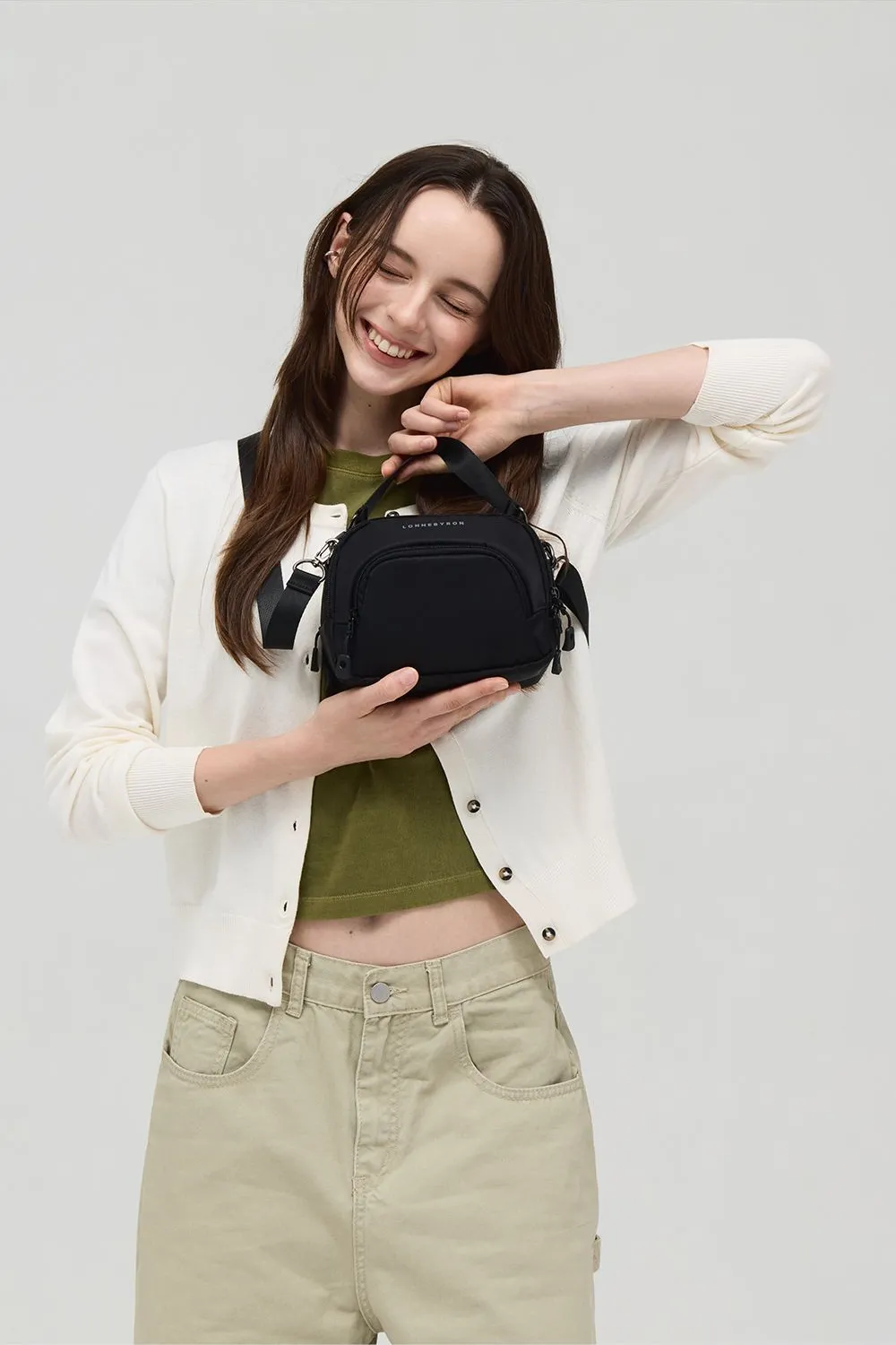 사은품 가방 안내 사진, 타코백 플러스, 흰 카디건 차림 여성이 검은 가방을 손으로 감싸 안은 상반신